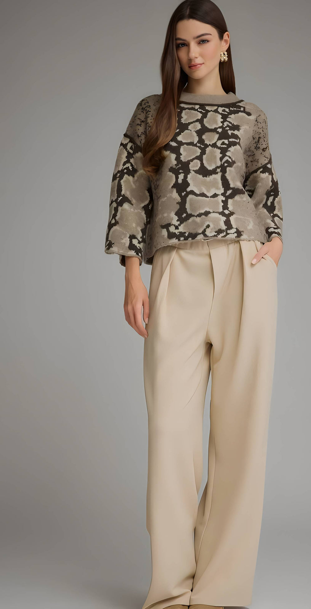 A woman modeling a beige and black snakeskin-patterned long-sleeve top paired with high-waisted, wide-leg beige trousers, set against a solid gray studio background.