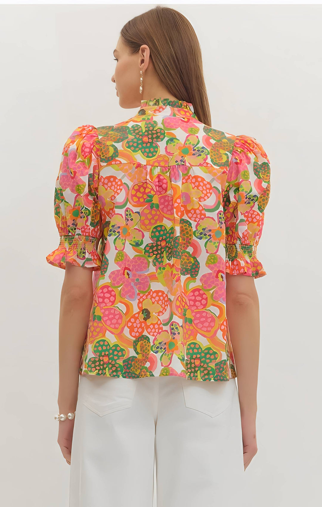Woman wearing a colorful floral blouse with white pants on a plain background