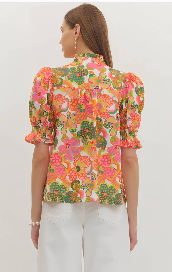 Woman wearing a colorful floral blouse with white pants on a plain background