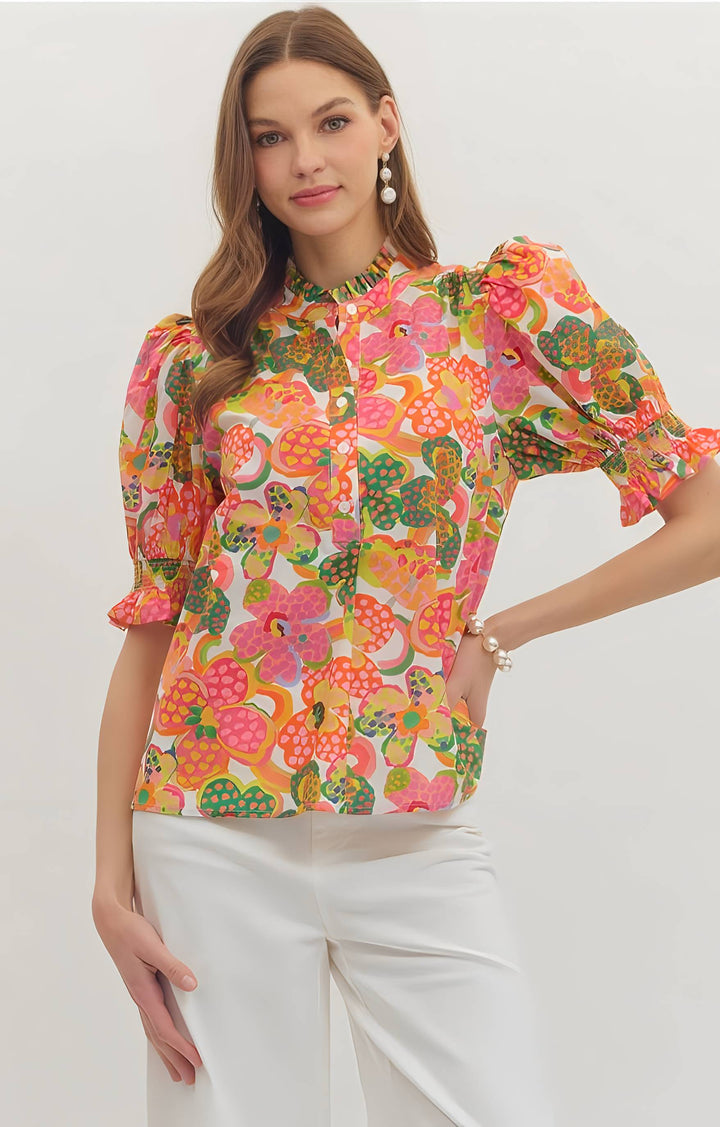 Woman wearing a colorful floral blouse with white pants on a light background