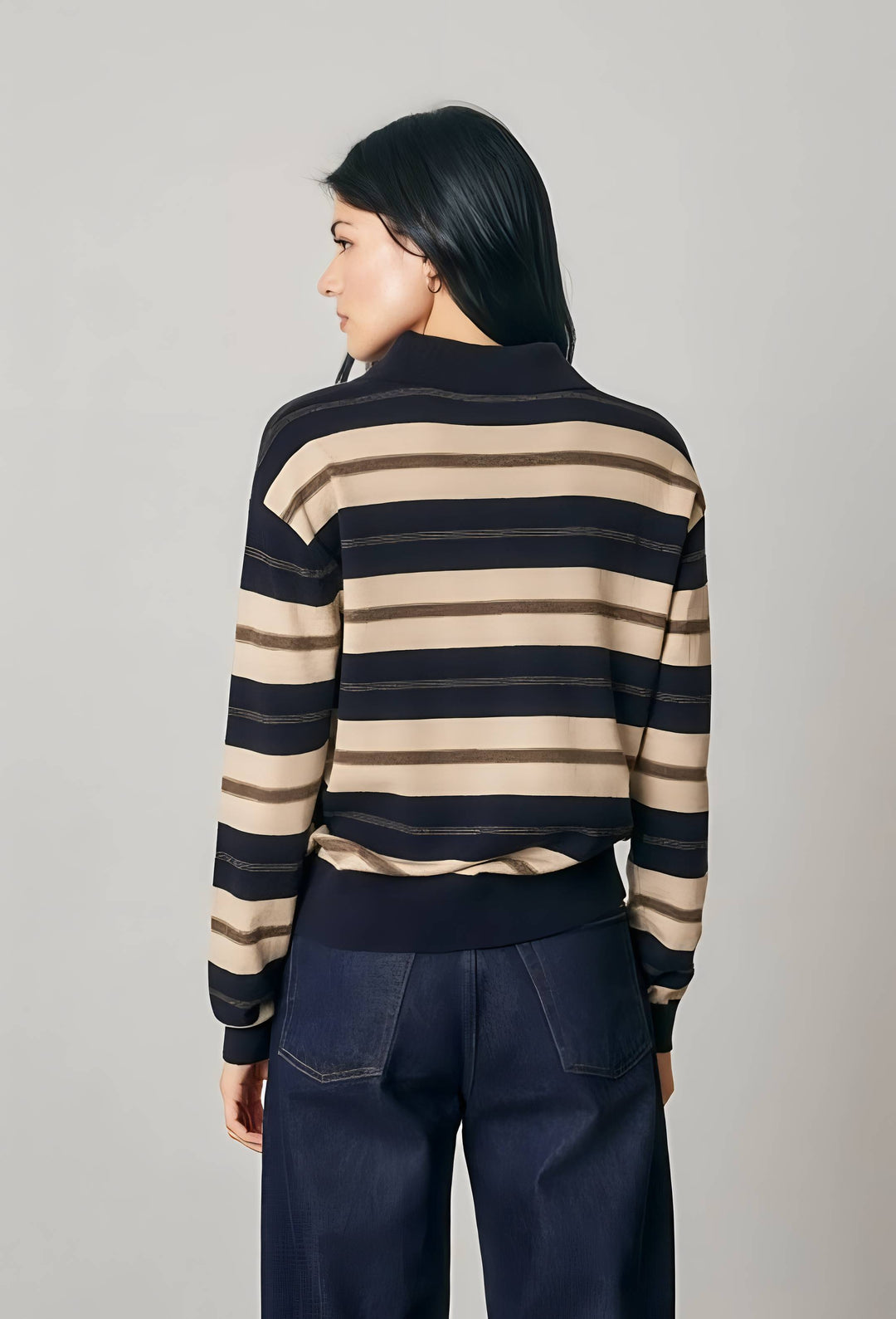 A woman shown from the back wearing a navy and beige horizontally striped knit sweater and dark navy wide-leg pants, photographed against a plain light gray studio background.