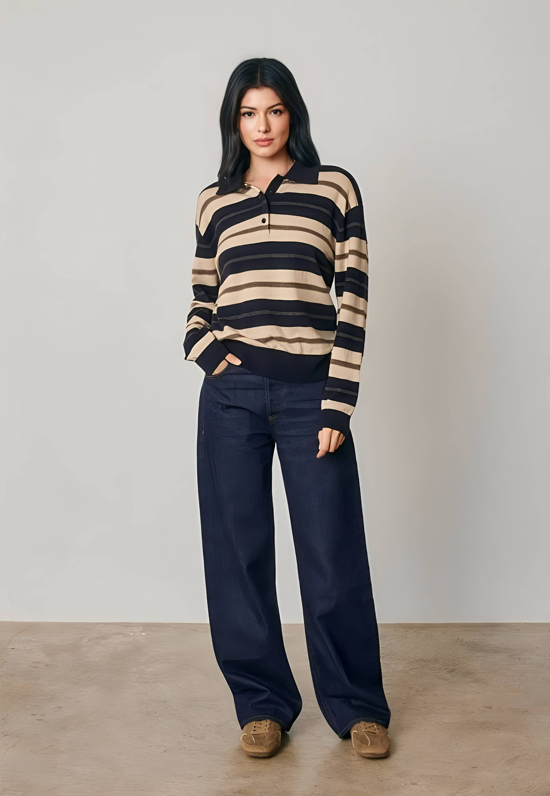 A woman modeling a long-sleeve knit polo sweater with horizontal beige and black stripes, paired with dark navy wide-leg trousers and brown suede shoes, set against a neutral studio backdrop.