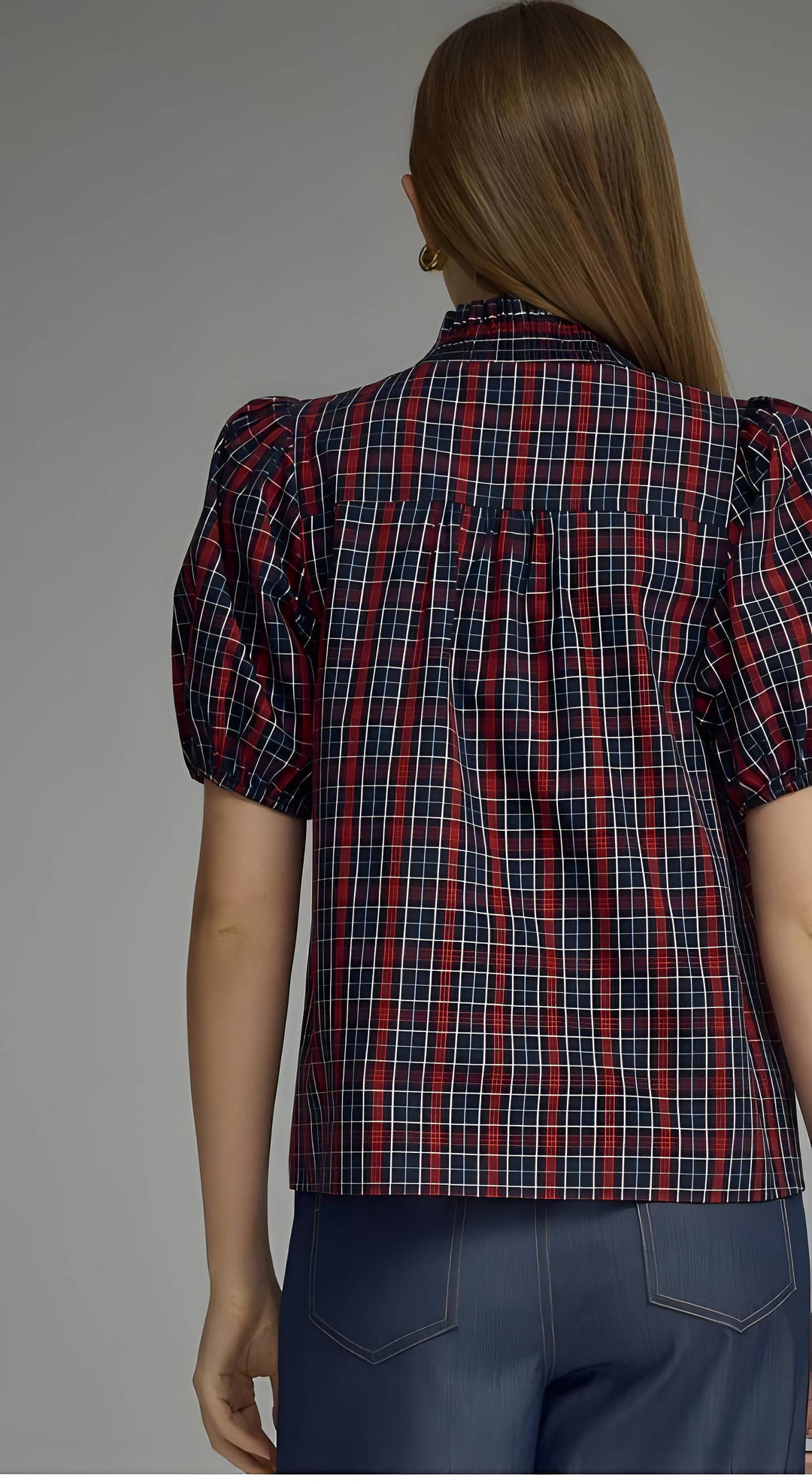 A woman shown from the back wearing a red, navy, and white plaid puff-sleeve blouse with dark blue jeans, set against a plain gray studio background.
