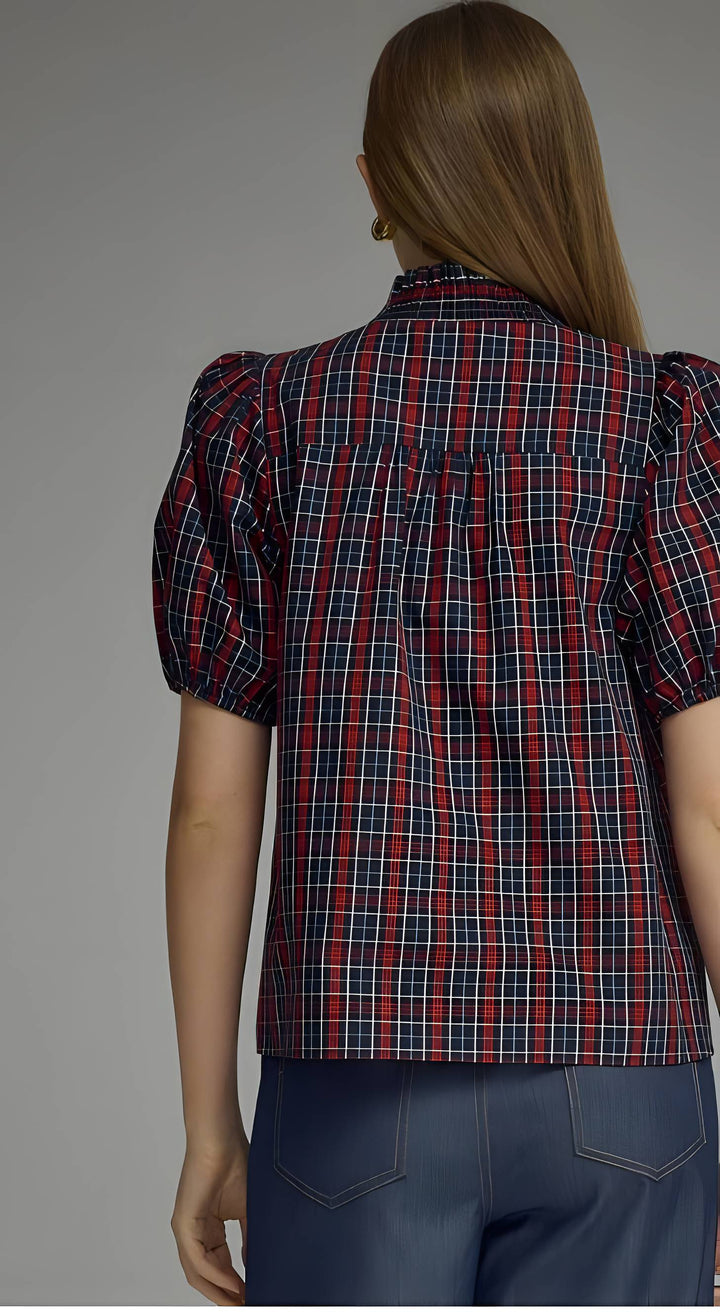 A woman shown from the back wearing a red, navy, and white plaid puff-sleeve blouse with dark blue jeans, set against a plain gray studio background.