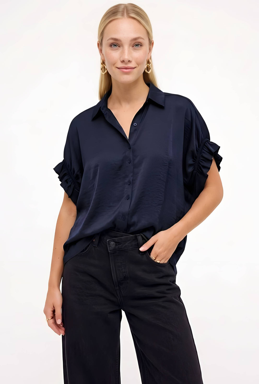 A woman modeling a black short-sleeve button-up blouse with ruffled cuffs, paired with black pants, against a plain white studio background.