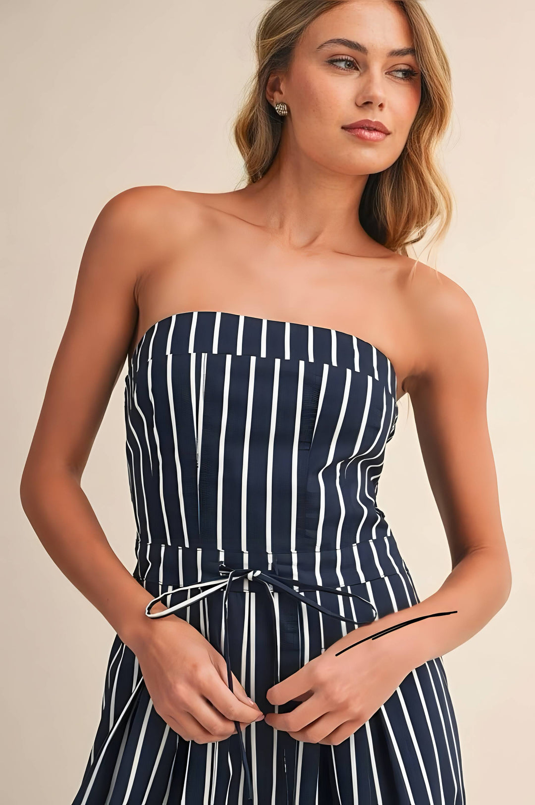 Woman wearing a strapless navy and white striped dress against a beige background