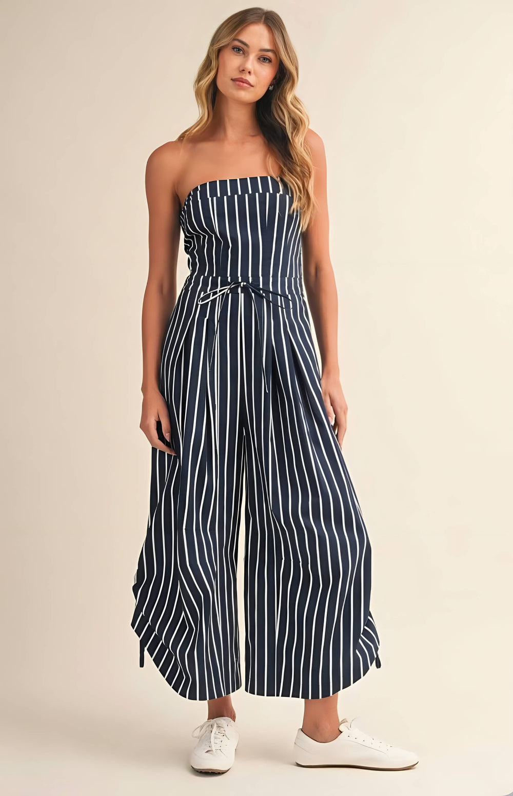 Woman wearing a strapless navy and white striped jumpsuit on a beige background
