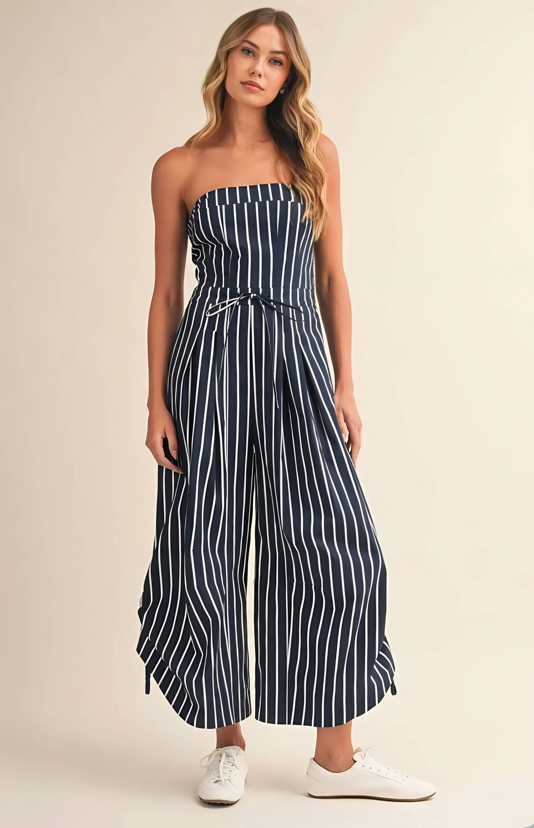 Woman wearing a strapless navy and white striped jumpsuit on a beige background