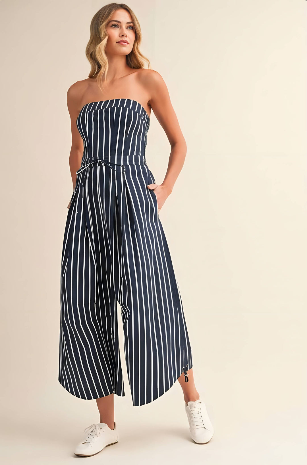 Woman wearing a strapless navy and white striped jumpsuit on a beige background