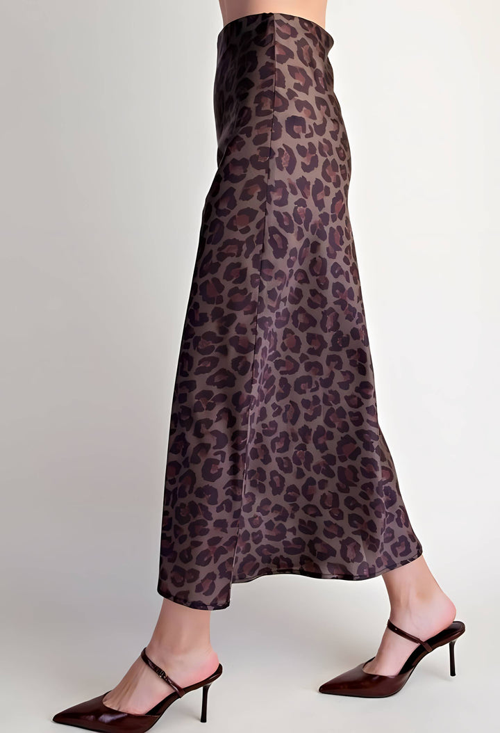 A model's lower body wearing a leopard print maxi skirt in brown and purple tones, paired with dark brown pointed-toe mule heels, against a plain light gray background.