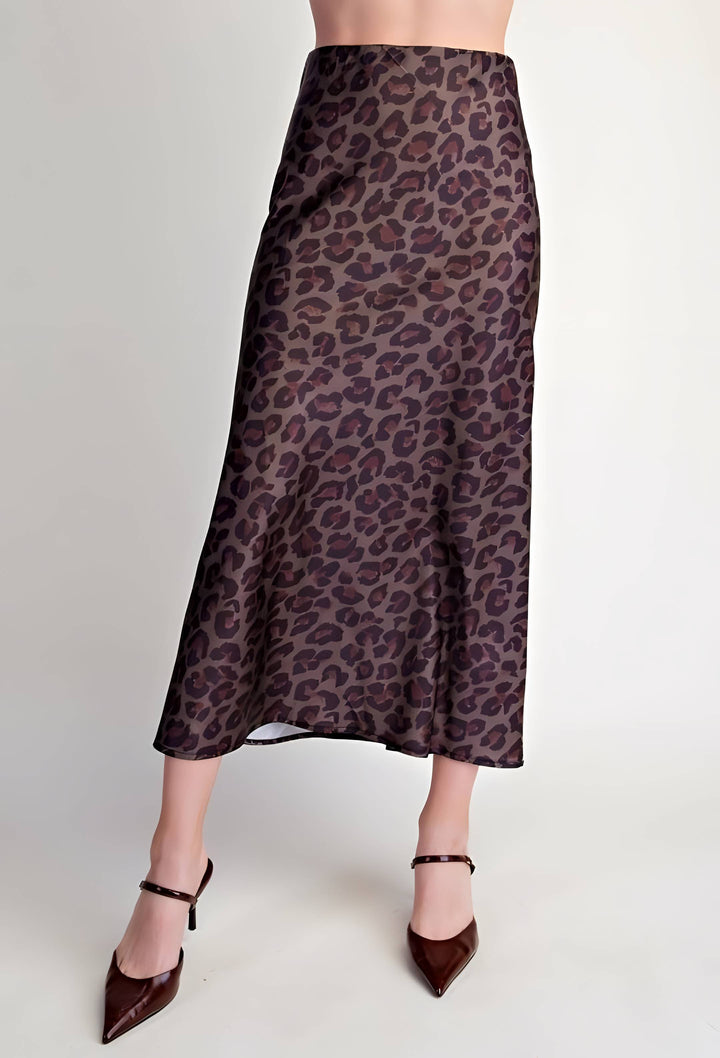 A model is shown from the waist down wearing a leopard print midi skirt in brown and purple tones, paired with dark brown pointed-toe heels, against a plain light gray studio background.