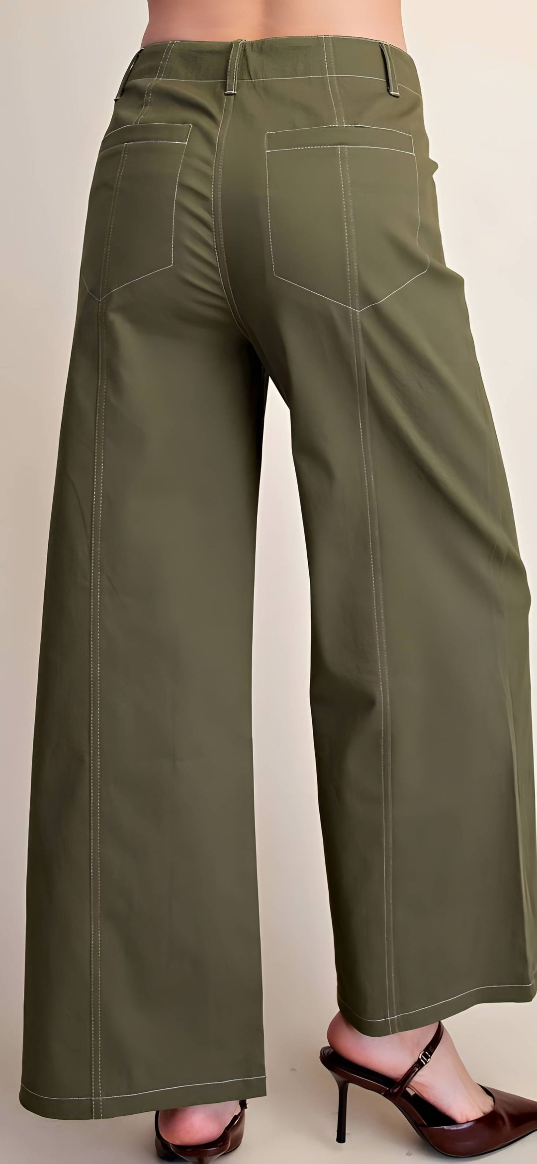 Olive green wide-leg pants shown from the back on a model, featuring contrast light stitching and back patch pockets, paired with dark brown heeled sandals.