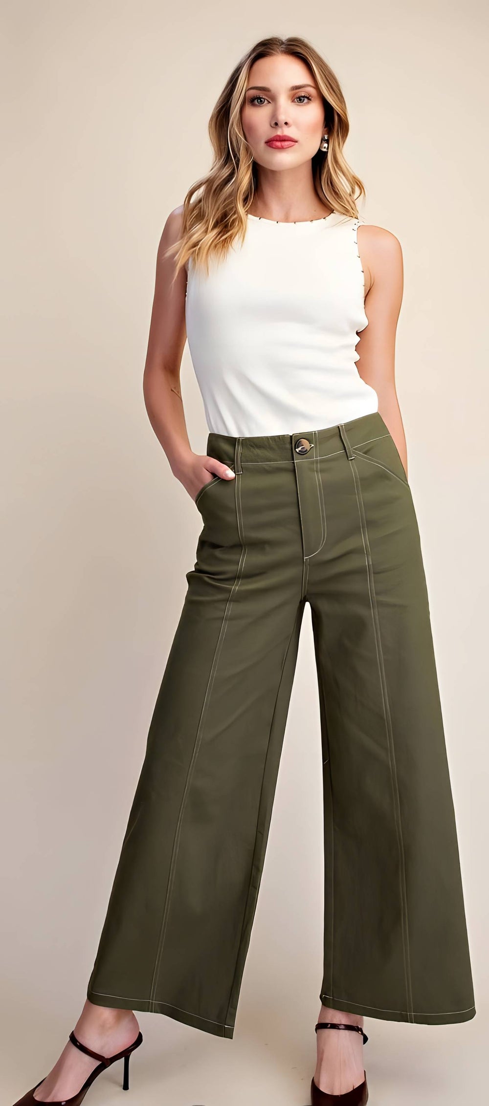 A woman modeling olive green wide-leg cropped pants with a white sleeveless top, standing against a solid beige studio background.