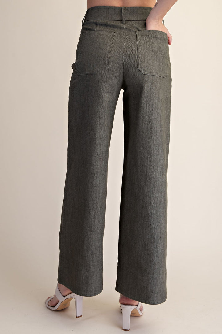 A person shown from the back wearing dark olive gray wide-leg cropped pants with side pockets, paired with white heeled sandals, against a plain beige studio background.