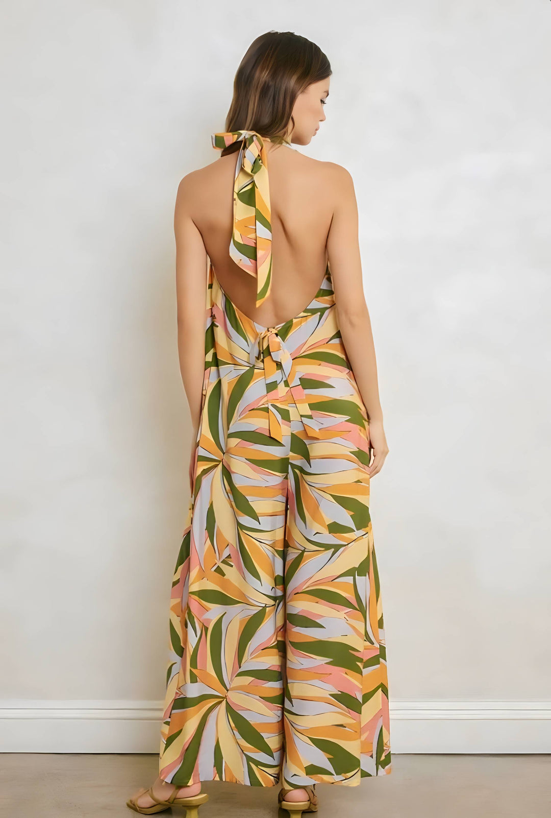 Woman wearing a colorful leaf-patterned jumpsuit against a white wall.