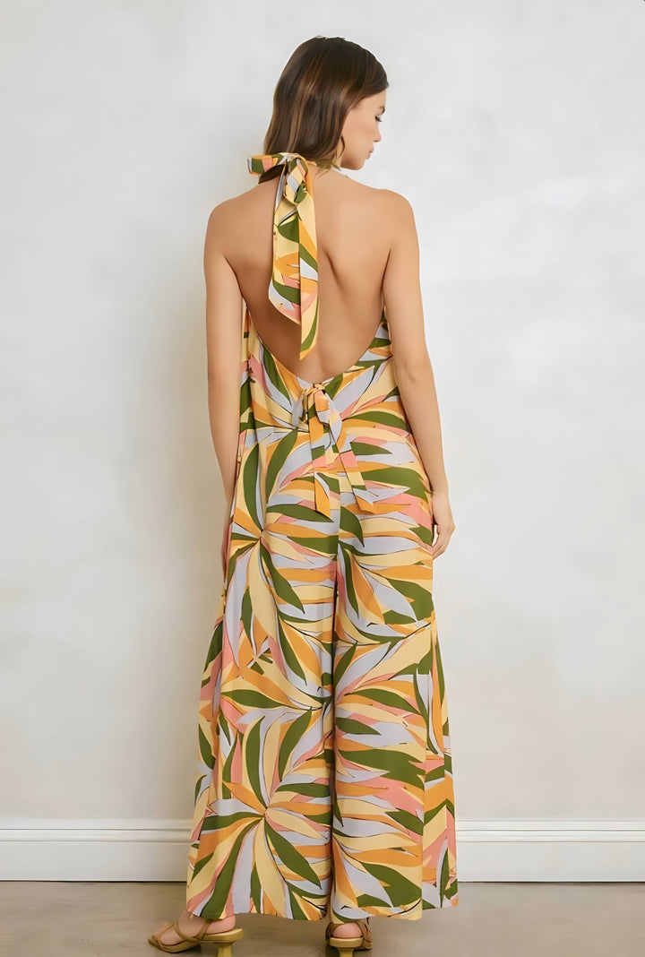 Woman wearing a colorful leaf-patterned jumpsuit against a white wall.