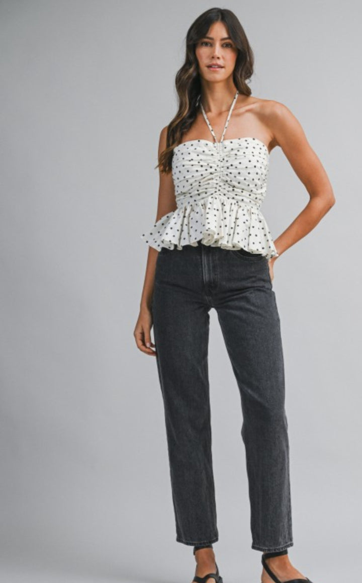 Woman wearing a white strapless top with black polka dots and dark jeans on a gray background
