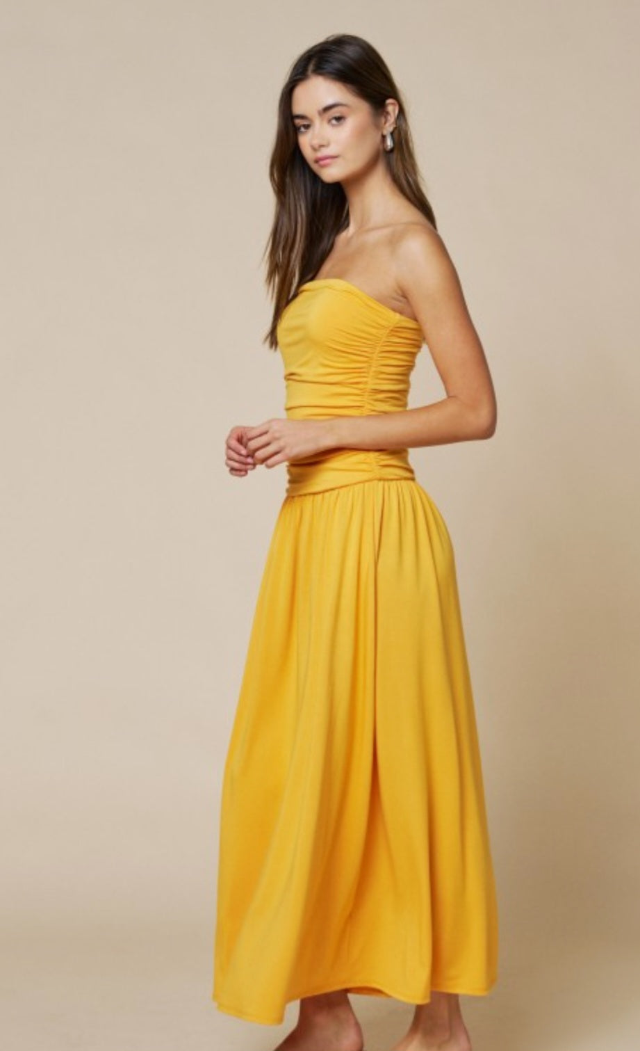 Woman wearing a yellow strapless dress against a beige background