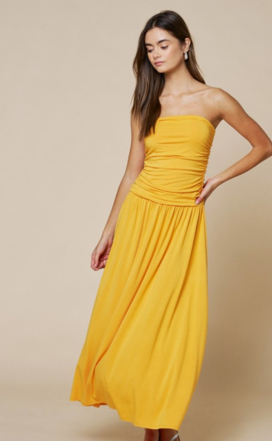 Woman wearing a yellow strapless dress against a beige background