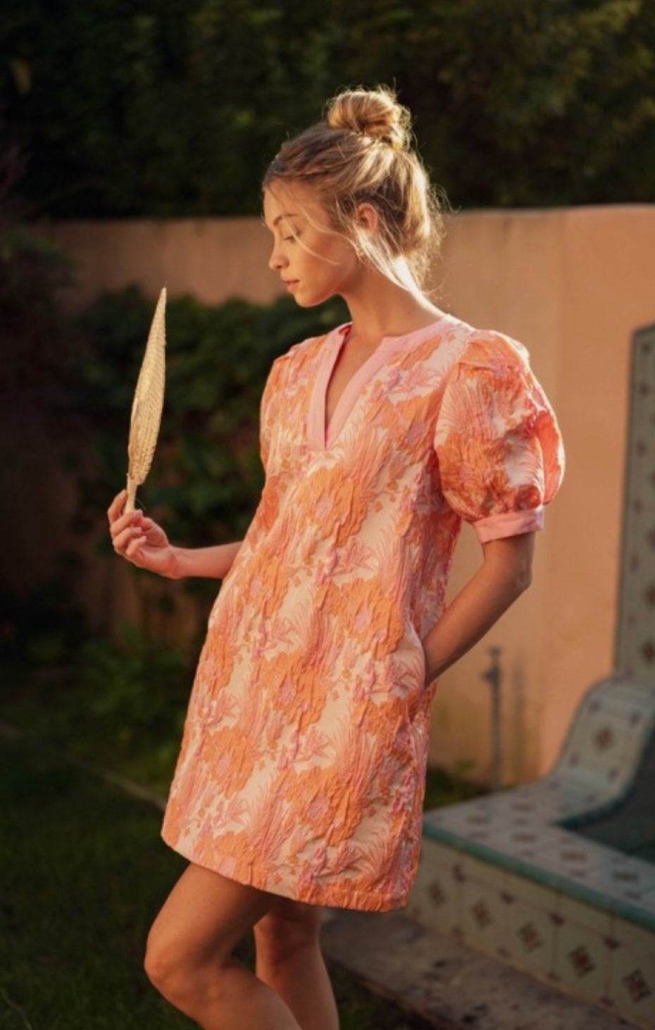 Woman in a floral dress holding a leaf in an outdoor setting