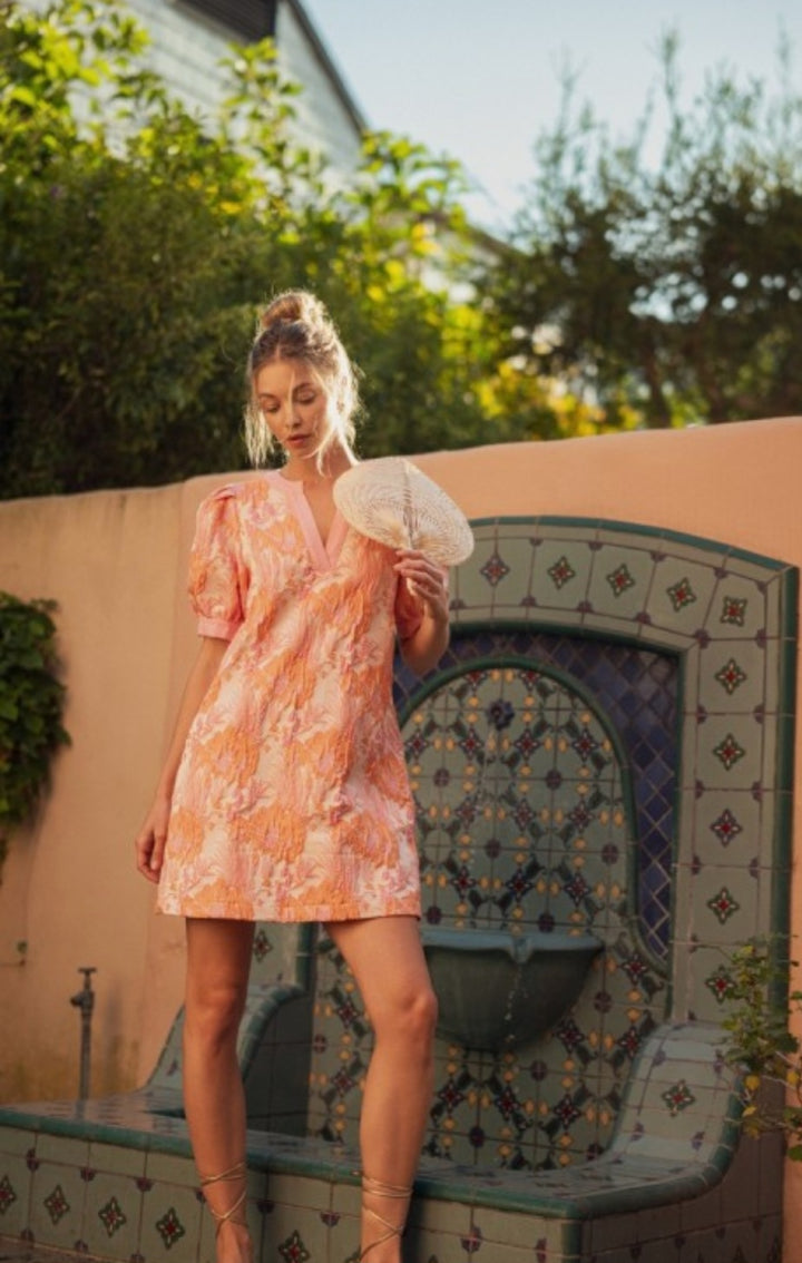 Woman in a floral dress standing next to a decorative fountain outdoors.