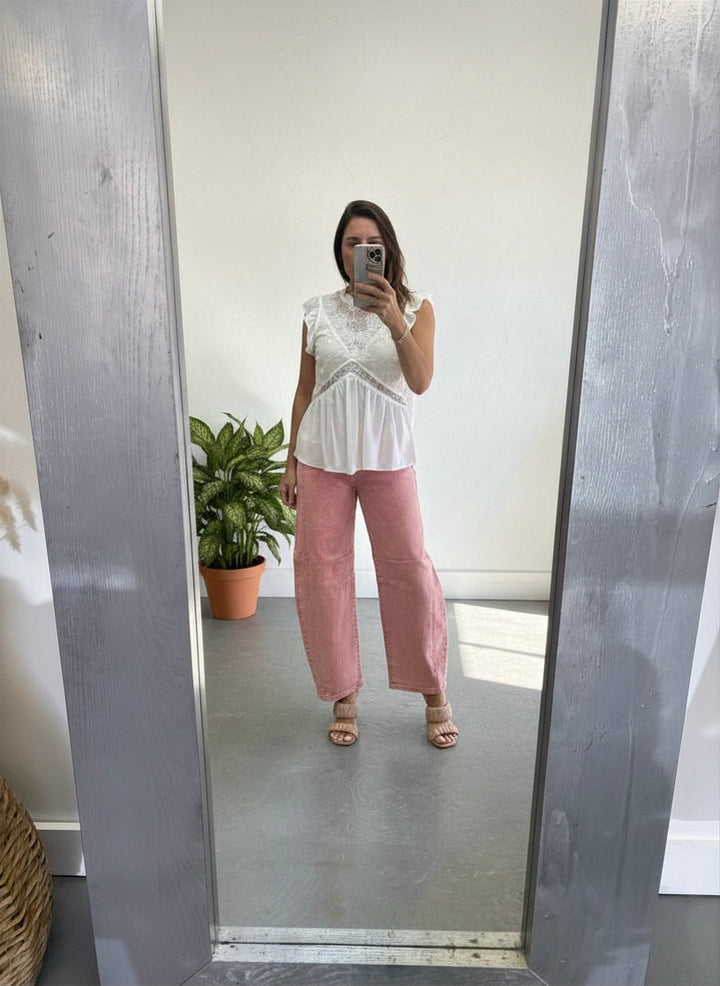 Person wearing a white top and pink pants standing in front of a mirror.
