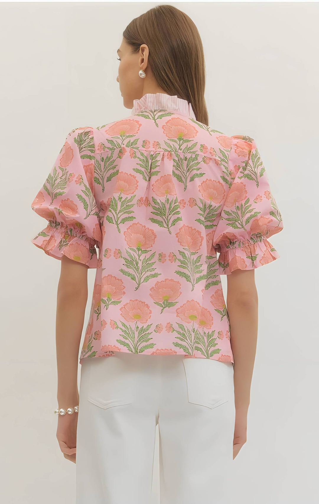 Woman wearing a pink floral blouse with white pants on a light background