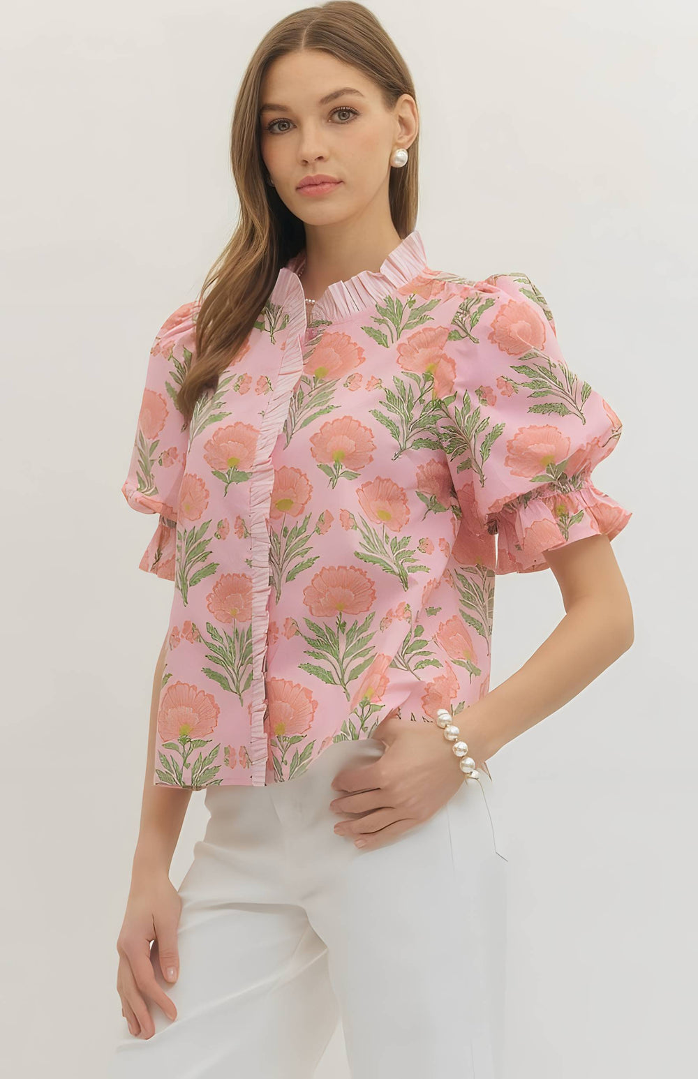 Woman wearing a pink floral blouse with white pants on a plain background