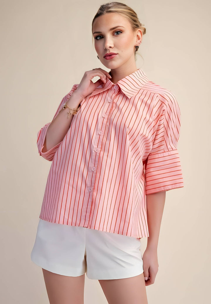 Woman wearing a pink striped shirt and white shorts against a beige background