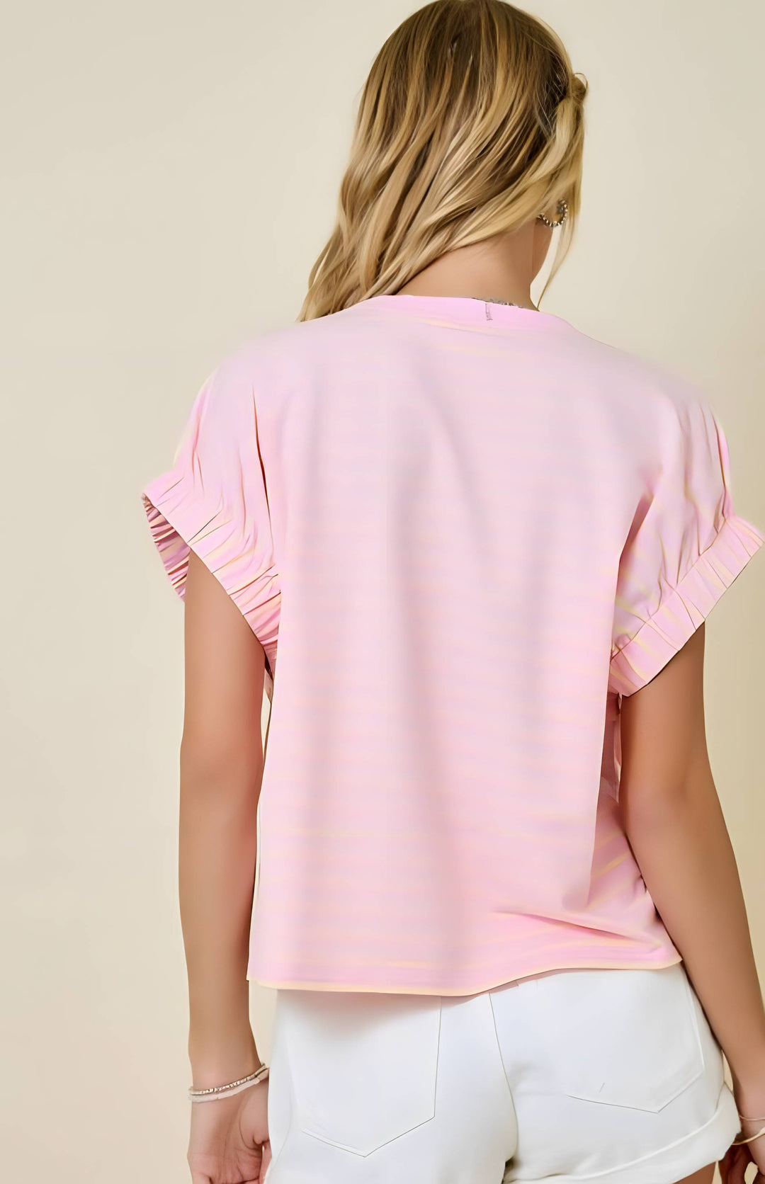 Person wearing a pink blouse with ruffled sleeves against a beige background