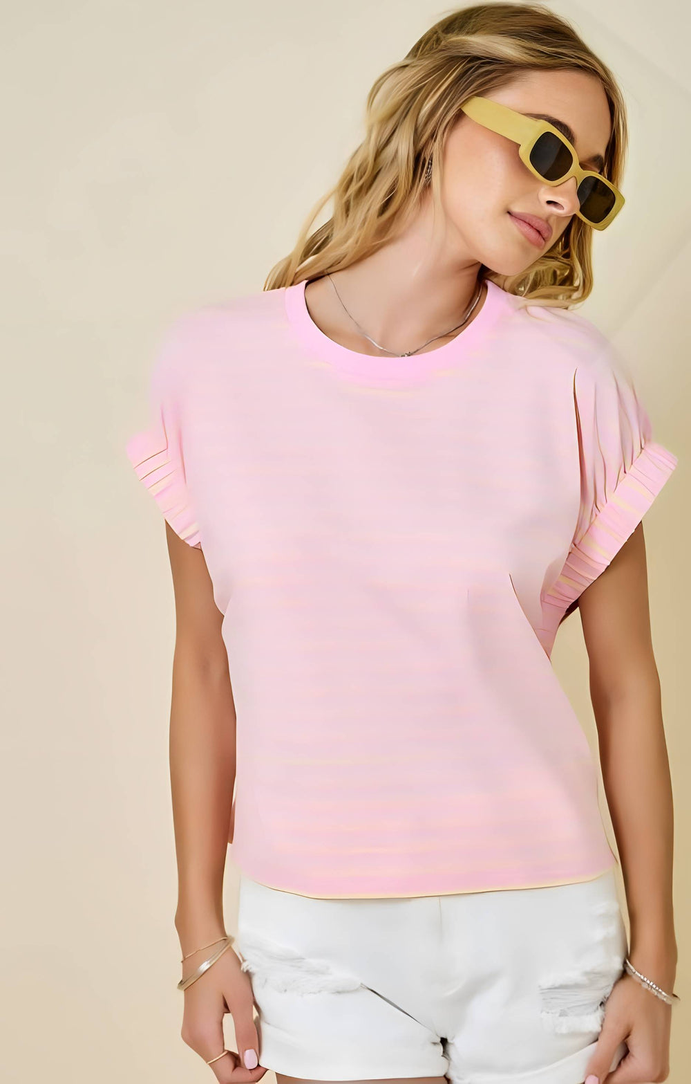 Woman wearing a pink top and white shorts with sunglasses on a beige background