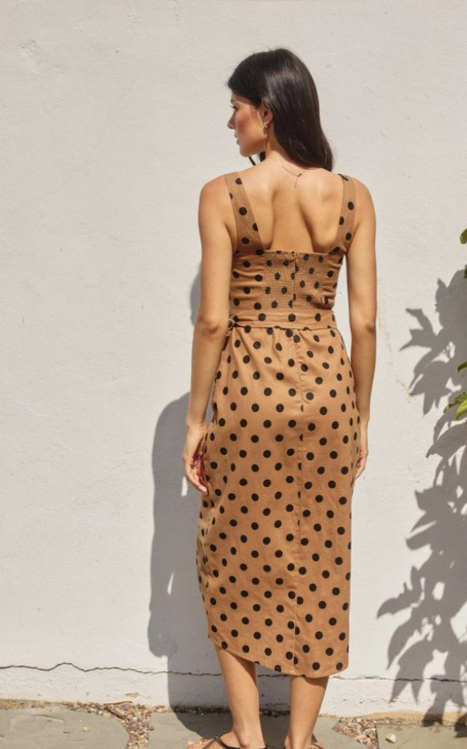 Woman wearing a brown dress with black polka dots against a white wall.