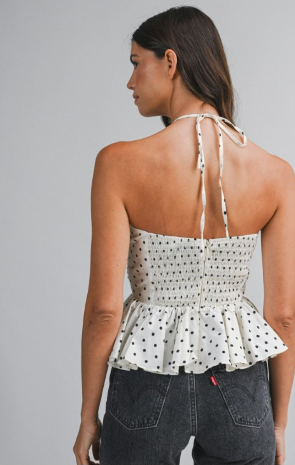 Woman wearing a polka dot top with thin straps on a gray background