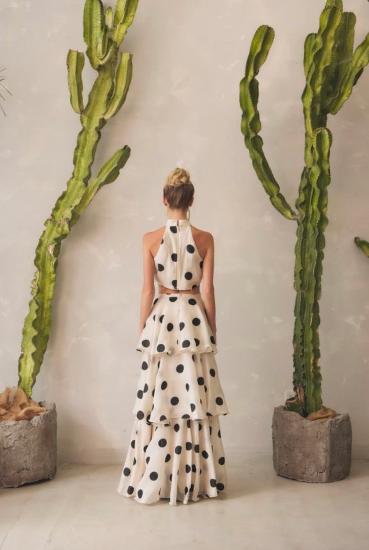 Woman in a polka dot dress standing between two tall cacti indoors.