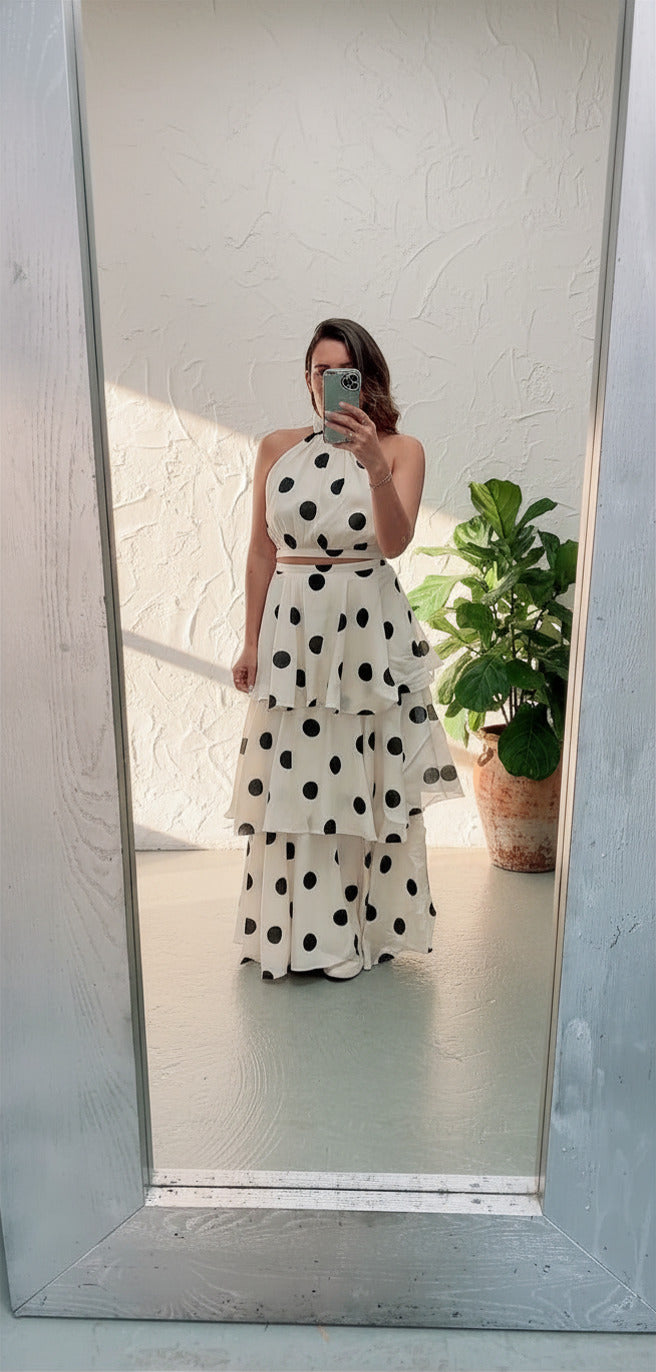 Woman taking a mirror selfie wearing a polka dot dress in a room with a plant.