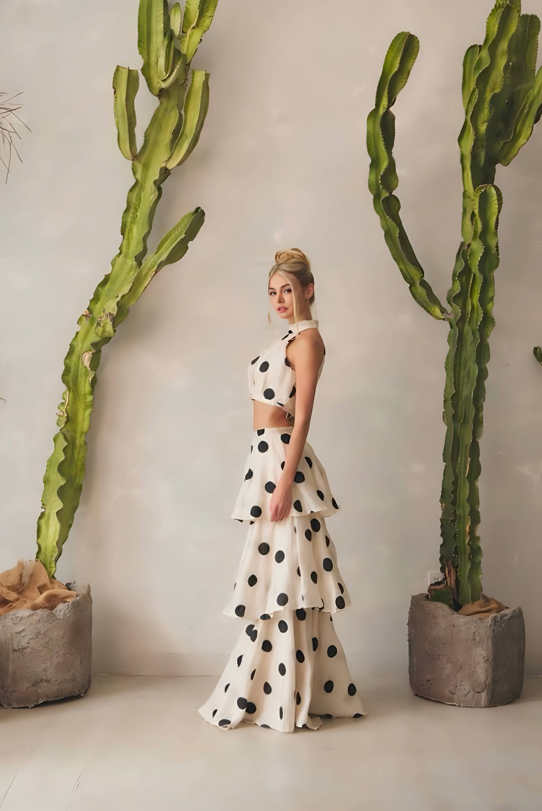 Woman in a polka dot dress standing between two large cacti indoors.