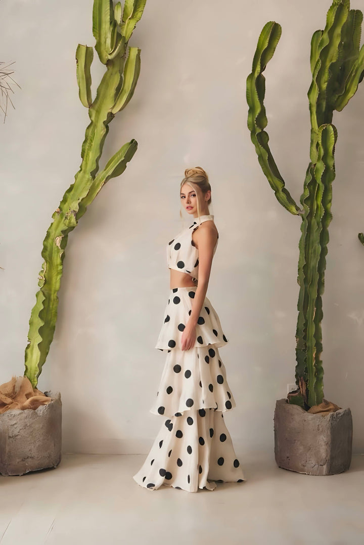 Woman in a polka dot dress standing between two large cacti indoors.