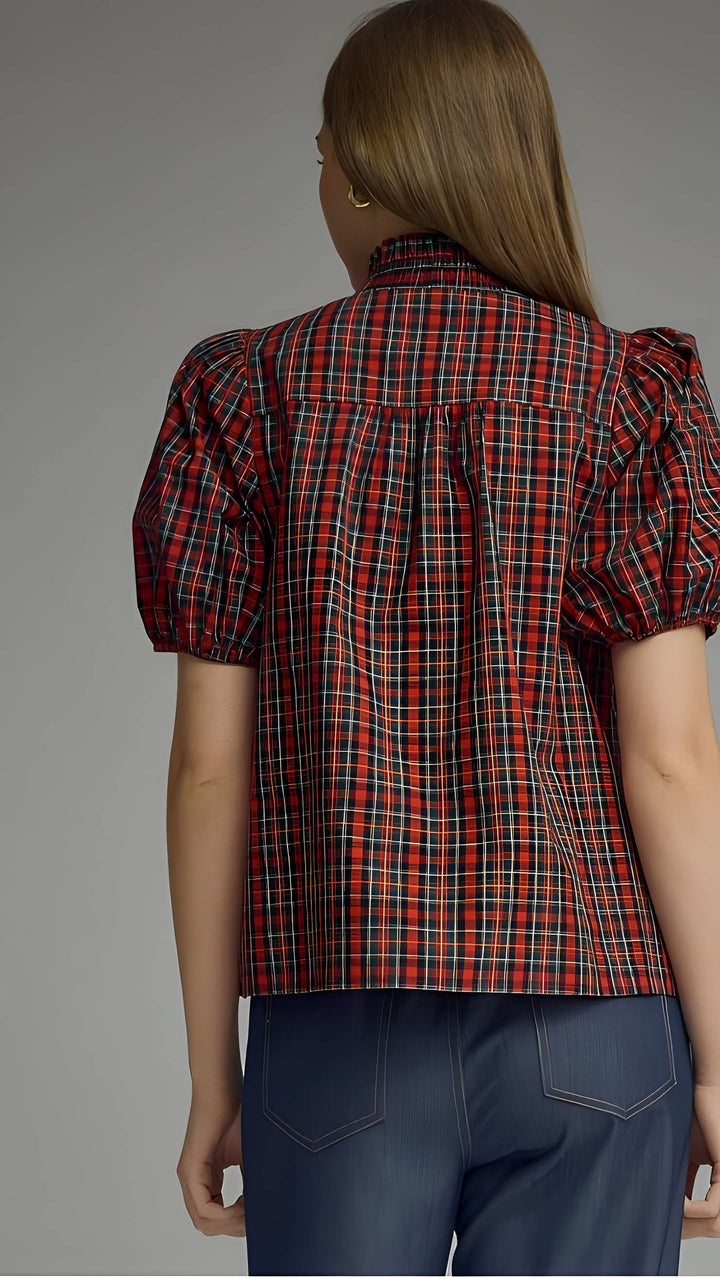 A woman shown from the back wearing a red and black plaid puff-sleeve blouse and dark blue jeans against a plain gray studio background.