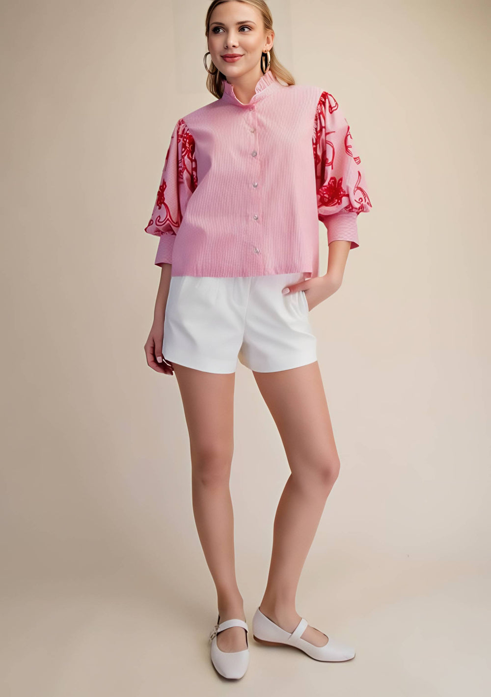 Woman wearing a pink blouse with red embroidery and white shorts on a beige background