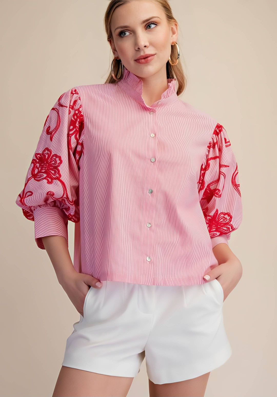 Woman wearing a pink blouse with red floral patterns and white shorts on a beige background