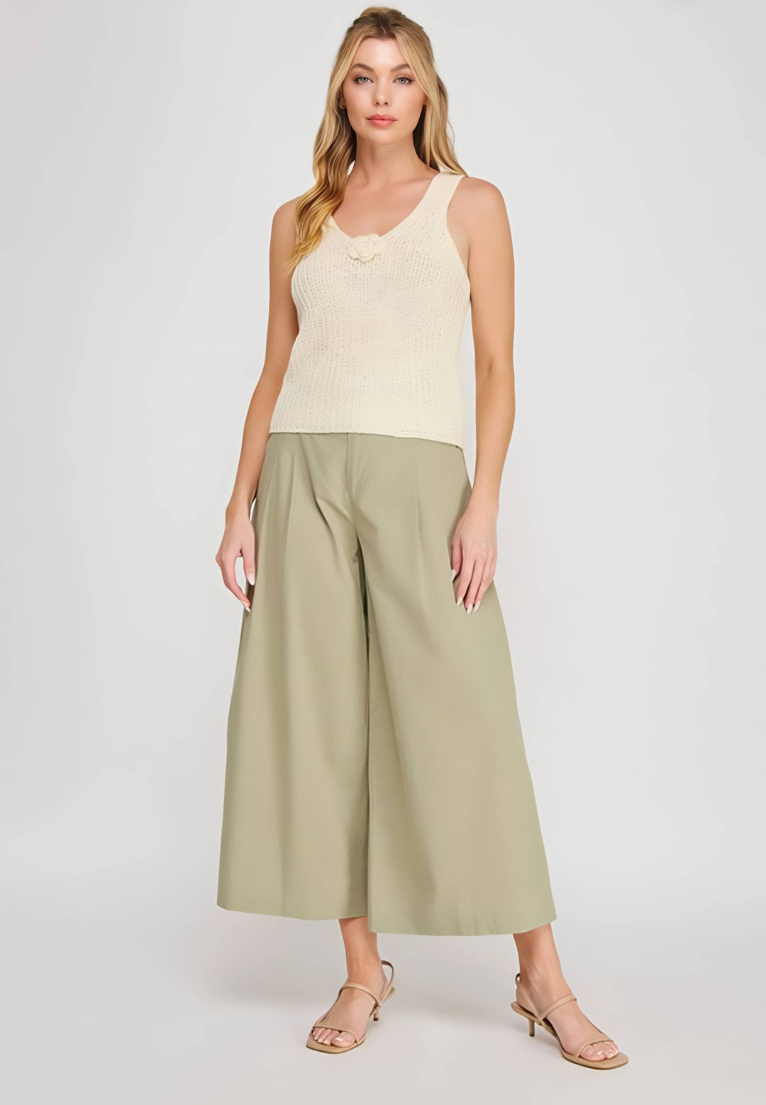 Woman wearing a beige sleeveless top and green wide-leg pants on a white background