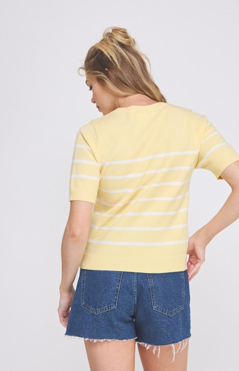 Woman wearing a yellow striped shirt and denim shorts on a white background