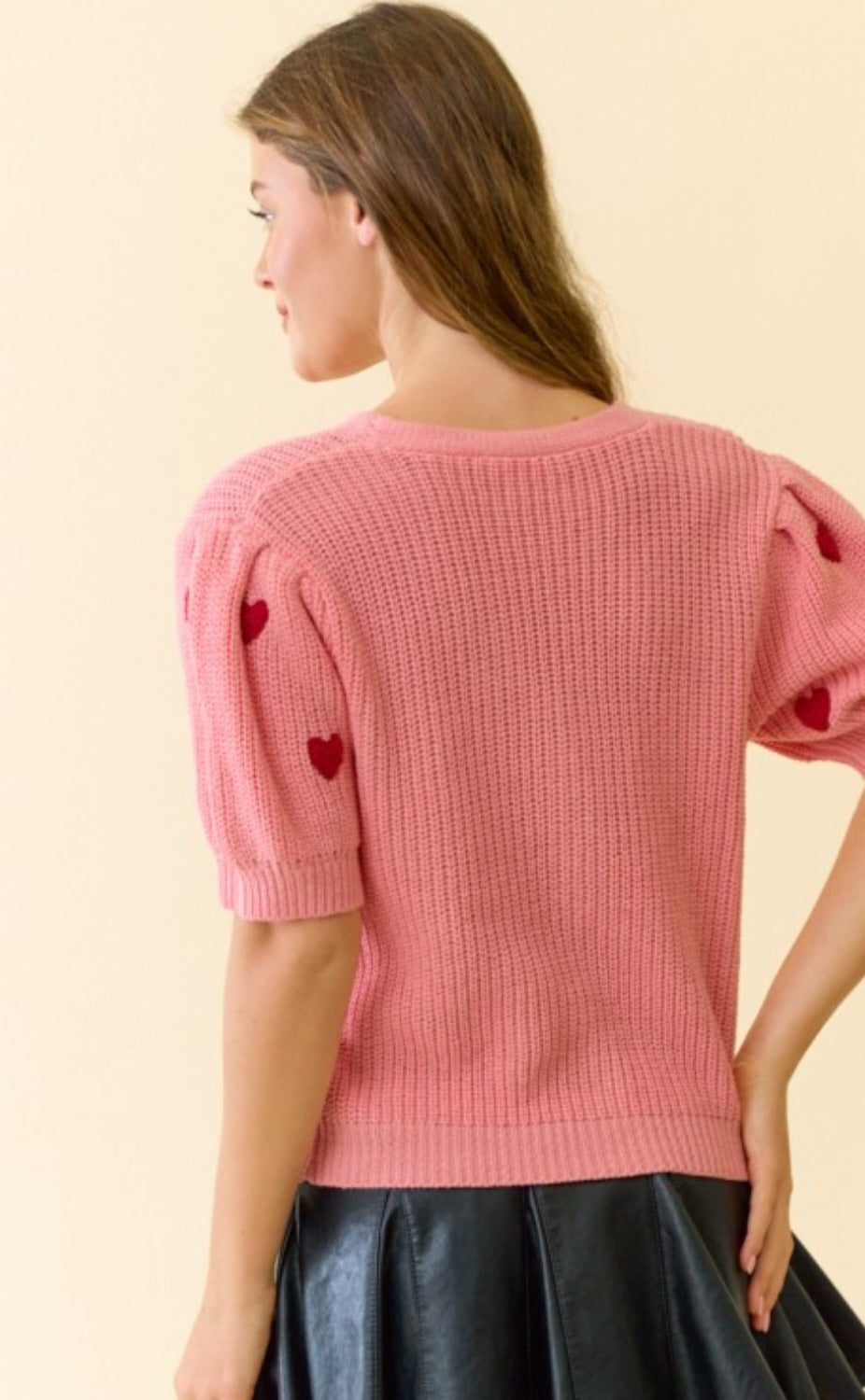 Woman wearing a pink knitted top with heart details on a beige background