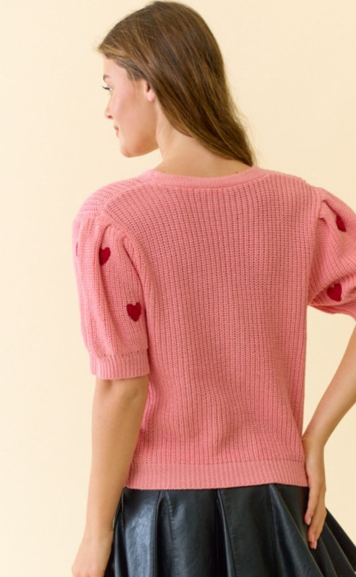 Woman wearing a pink knitted top with heart details on a beige background