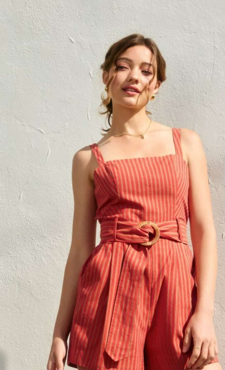 Model wearing an orange striped belted romper with sleeveless design, cinched waist, and relaxed-fit shorts – vibrant and lightweight outfit perfect for summer or vacation wear.