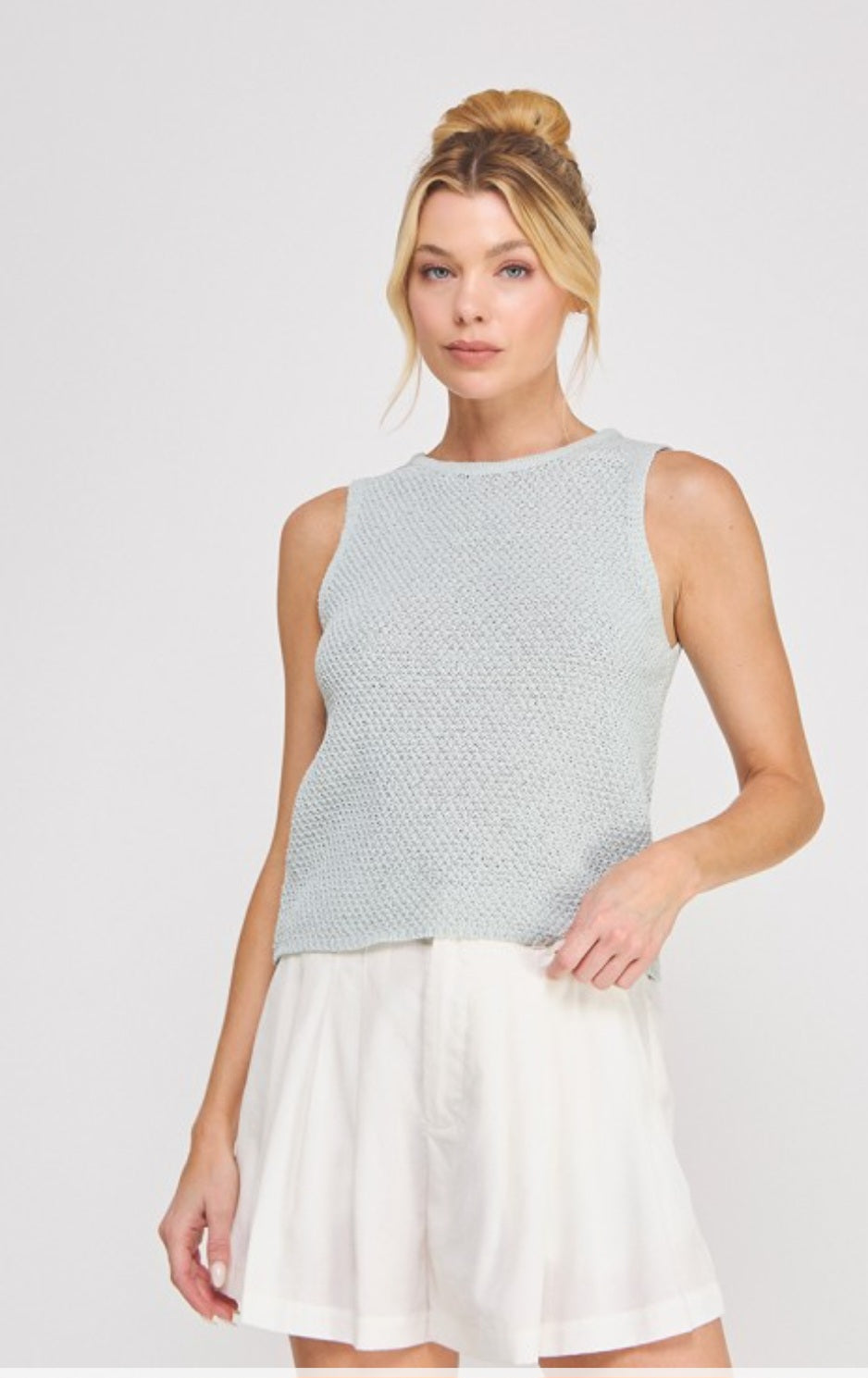 Woman wearing a light blue sleeveless top and white skirt on a gray background