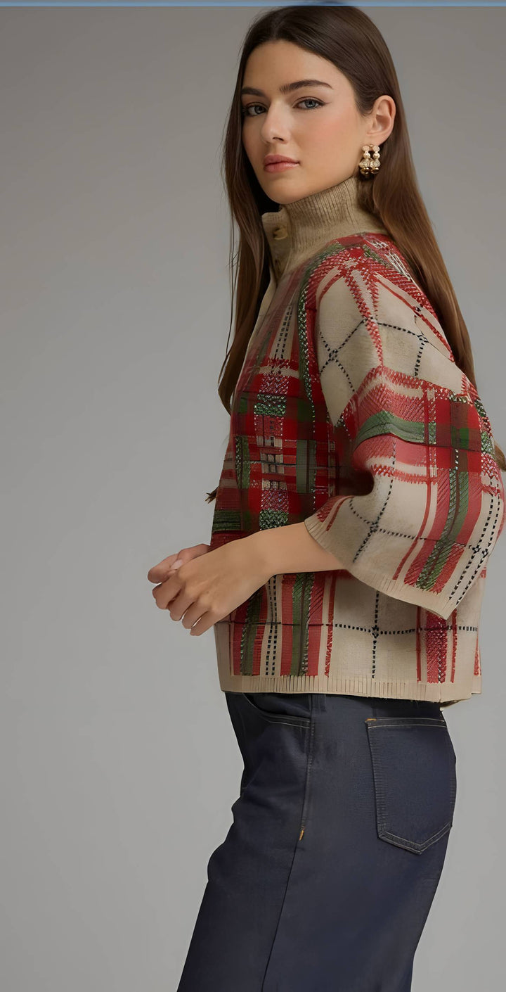 A woman modeling a cropped, turtleneck knit sweater with a red, green, and beige plaid pattern, paired with dark blue jeans against a solid gray studio background.