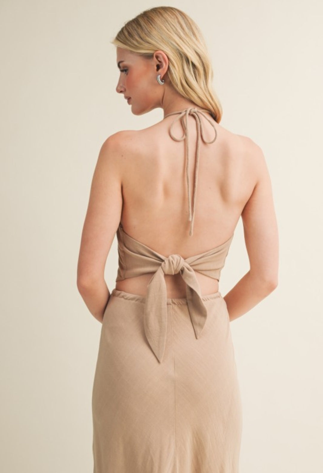 Woman wearing a beige halter neck top with bow details on a plain background