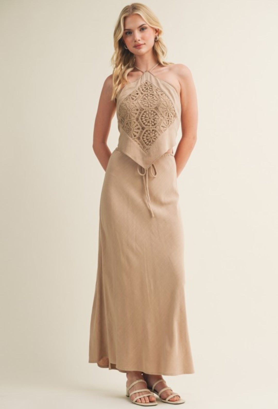 Woman wearing a beige dress with lace detailing on a plain background