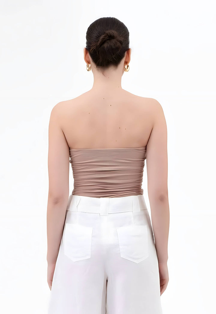 A woman shown from the back wearing a strapless ruched tube top in taupe and white pants, against a plain white studio background.